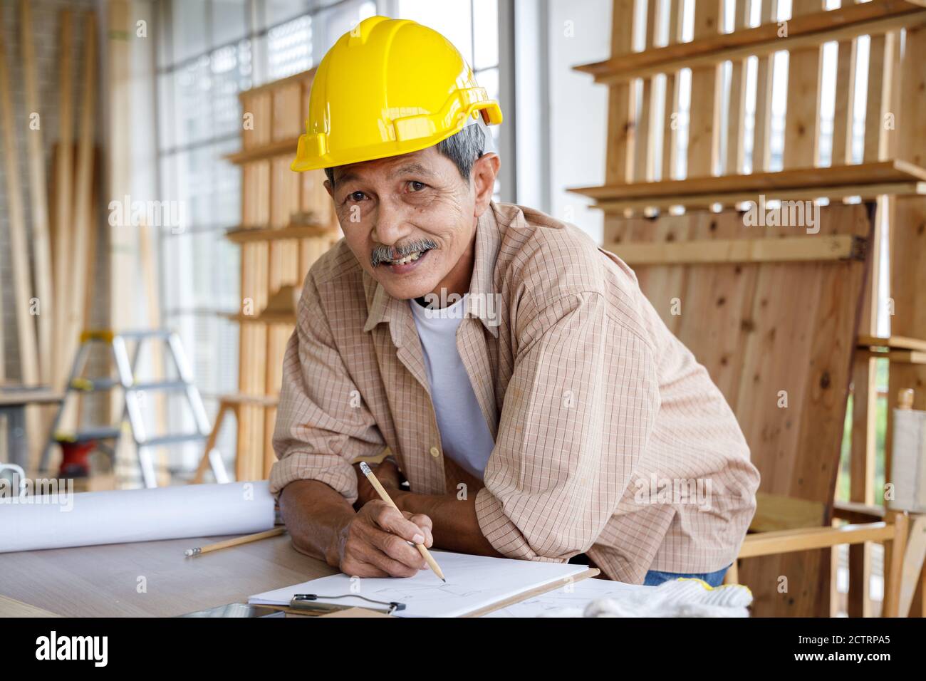 Happy Asian alter Mann mit Sicherheitshelm Arbeit in Schreinerei Werkstatt. Konzept Senioren Hobby nach dem Ruhestand. Stockfoto