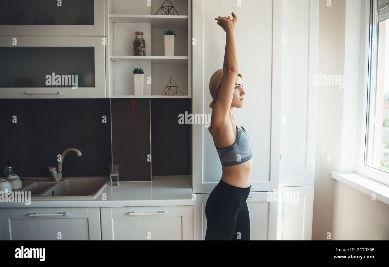 Junge kaukasische blonde Frau in Sportswear ist immer bereit für Digitale Fitness zu Hause durch Dehnen und Aufwärmen Stockfoto