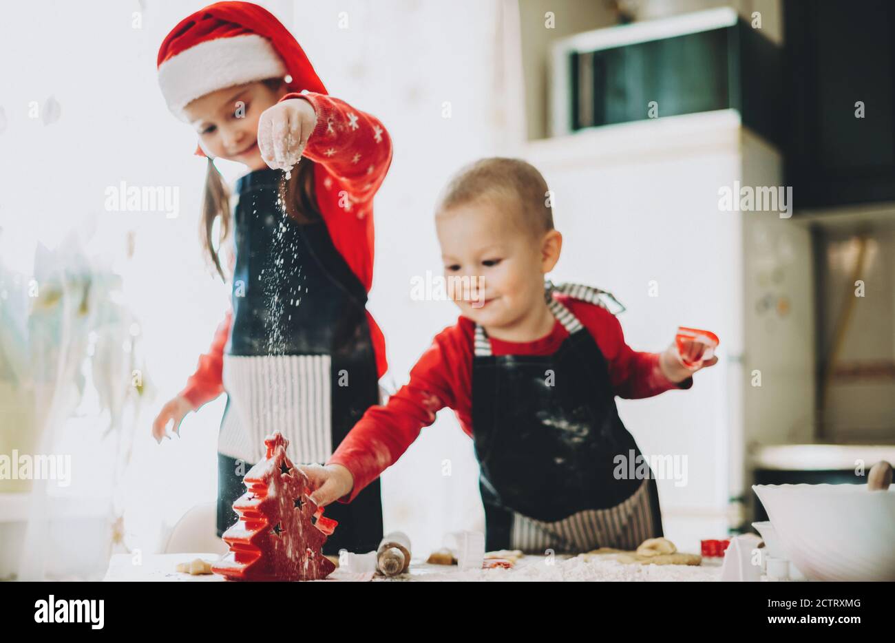 Weihnachten Vorbereitung von zwei Geschwistern machen Cookies in rot gekleidet Kleidung mit weihnachtsmütze Stockfoto