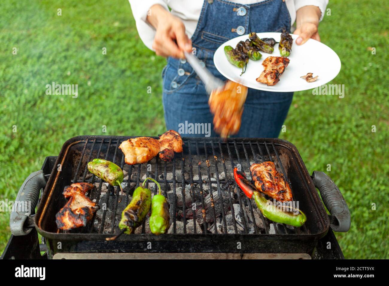 Ein Koch trägt jean Overalls und weißes Hemd ist von einem Holzkohlegrill, wo marinierte Hähnchenscheiben, rote und grüne Paprika sind Feuer gegrillt. Sie verwendet t Stockfoto