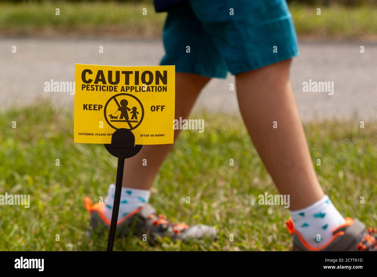 Clarksburg, MD, USA 09/12/2020: Ein gelbes Yard-Schild warnt Kinder und Haustiere vor dem jüngsten Pestizidspritzen und rät ihnen, fern zu bleiben. Ein Kind spielt Stockfoto