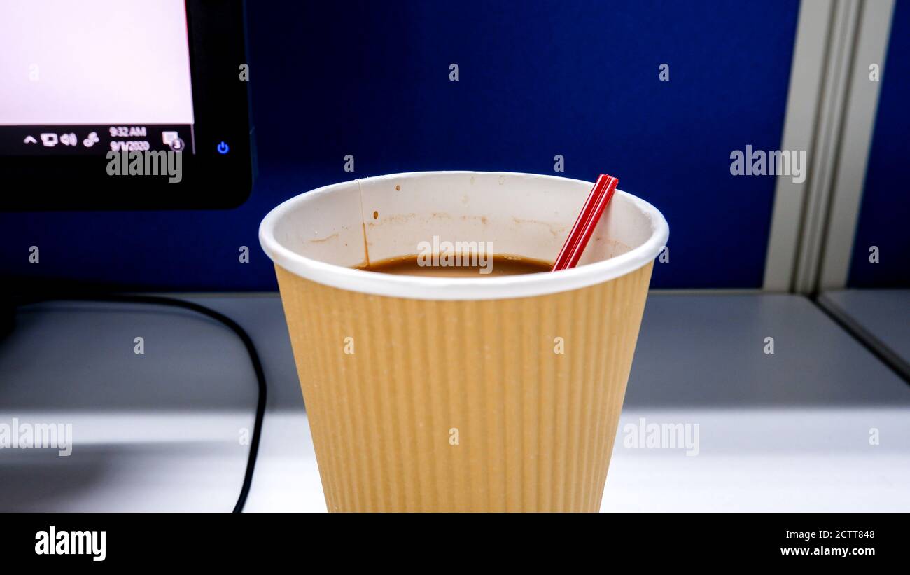 Nahaufnahme einer Einweg-Tasse Kaffee mit Rührwerk Auf dem Schreibtisch mit Computerhintergrund Stockfoto