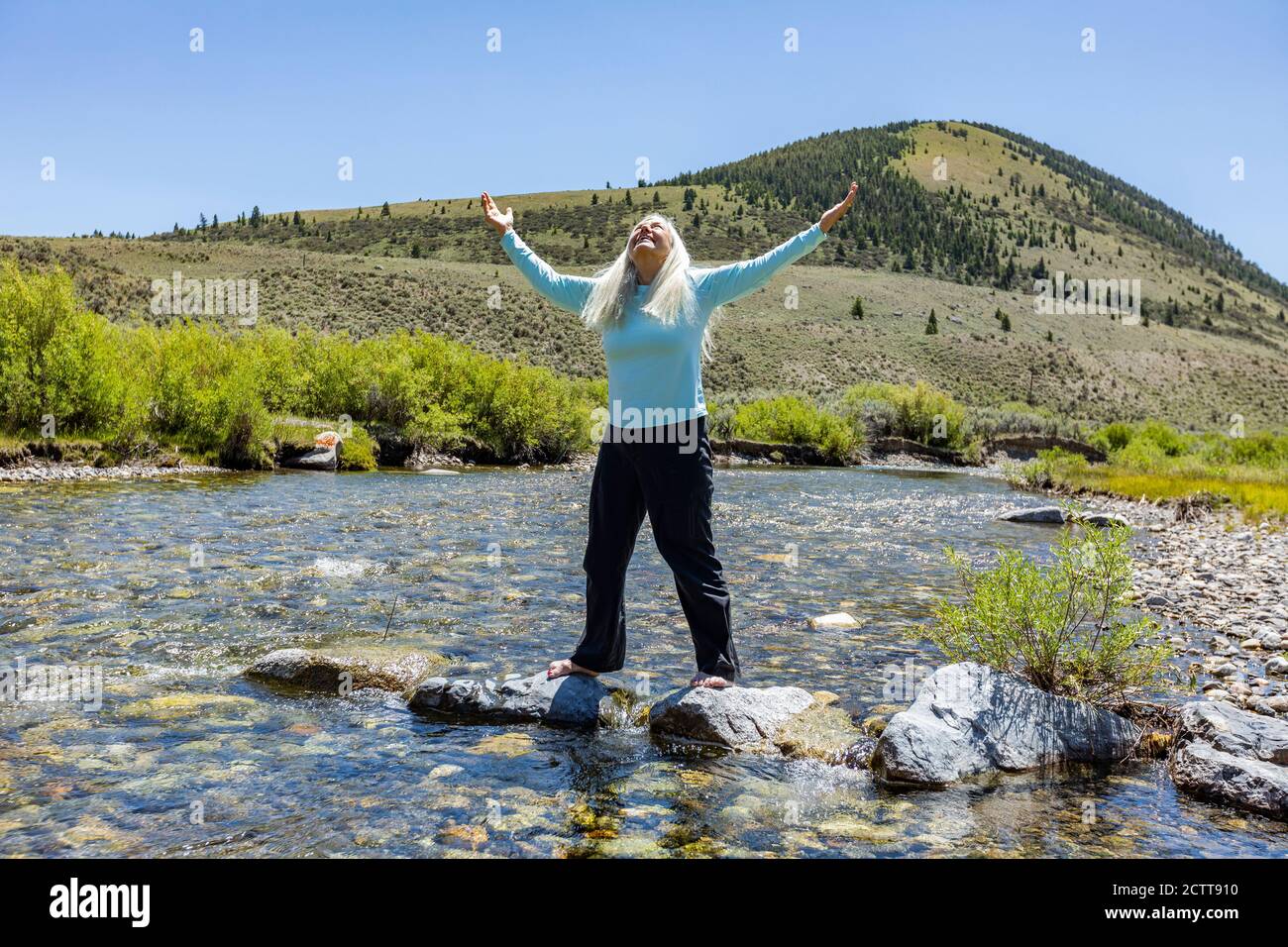 USA, Idaho, Sun Valley, Frau mit aufgehobenen Armen, die auf Felsen im Fluss stehen Stockfoto