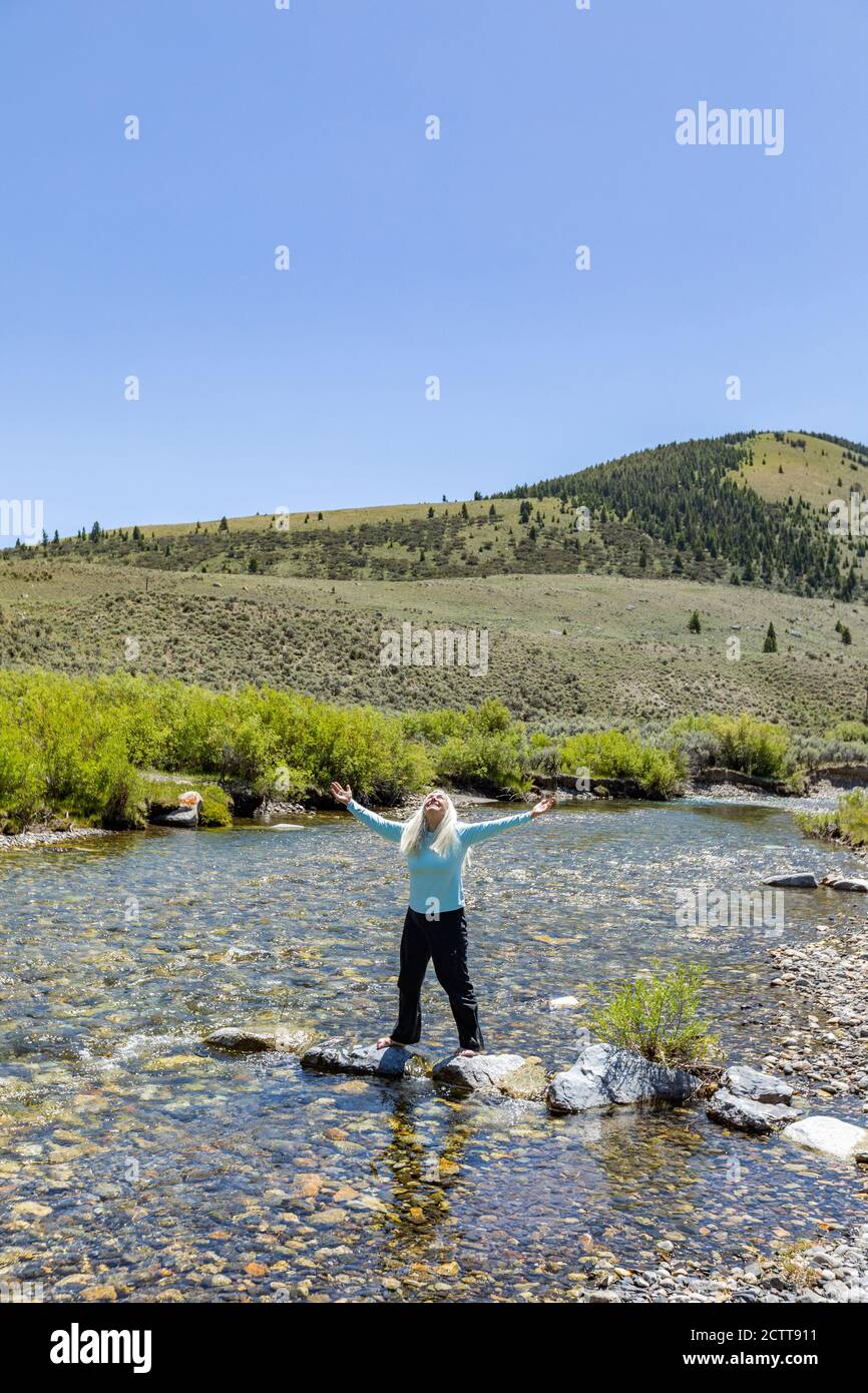 USA, Idaho, Sun Valley, Frau mit aufgehobenen Armen, die auf Felsen im Fluss stehen Stockfoto