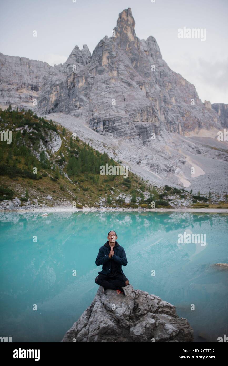 Italien, Südtirol, Cortina d Ampezzo, See Sorapis, Mann in Meditation Pose sitzt auf Felsen gegen See Stockfoto
