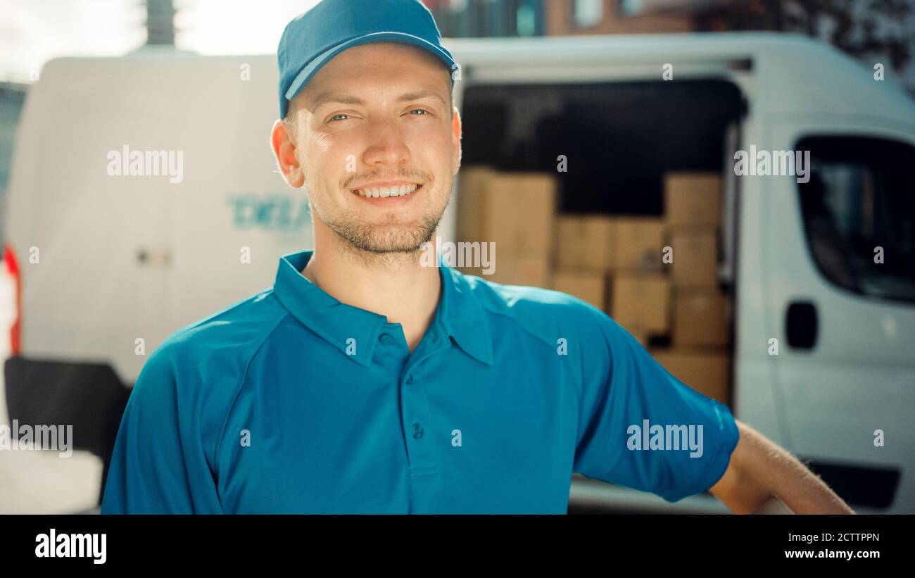 Portrait von Handsome Delivery man hält Karton-Box-Paket stehen in modernen stilvollen Business District mit Lieferwagen im Hintergrund. Lächelnd Stockfoto