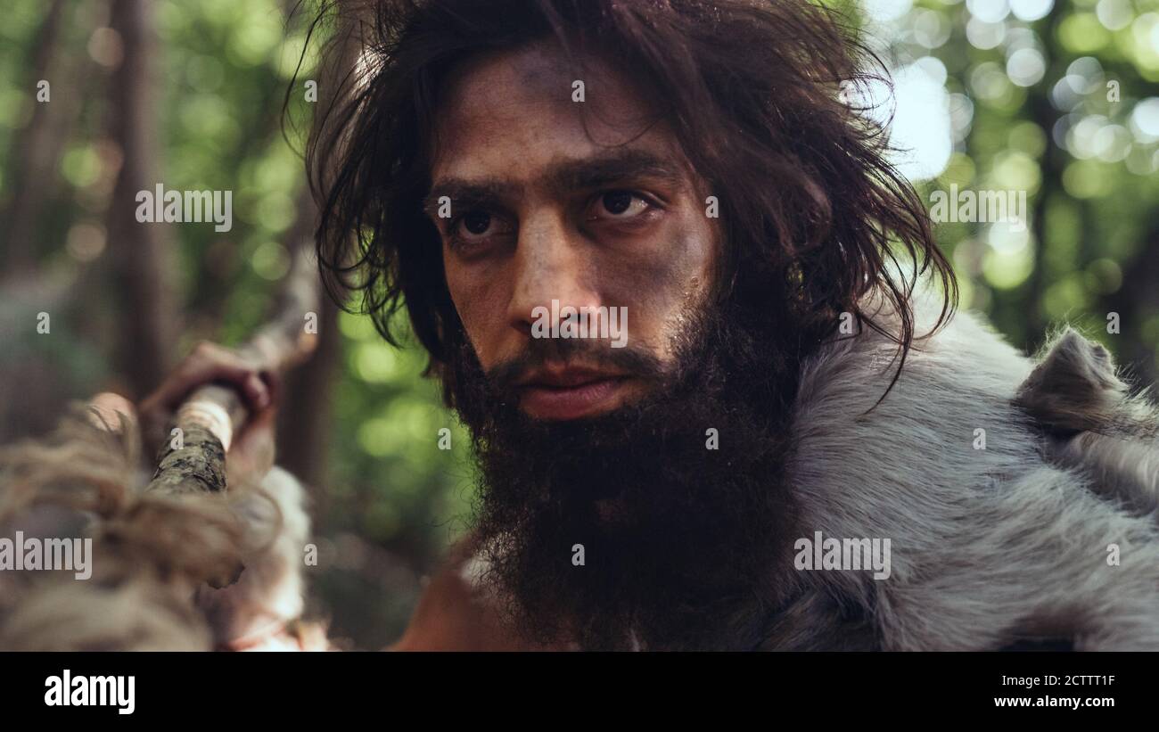 Portrait des urzeitlichen Höhlenmenschen in Tierhaut und Pelzjagd mit einem steinernen Speer im Urwald. Prähistorischer Neandertaler Jäger Stockfoto