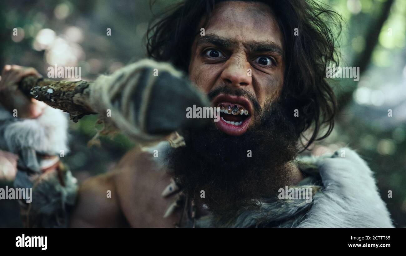 Portrait des urzeitlichen Höhlenmenschen in Tierhaut und Pelzjagd mit einem steinernen Speer im Urwald. Prähistorische Neandertaler Stockfoto