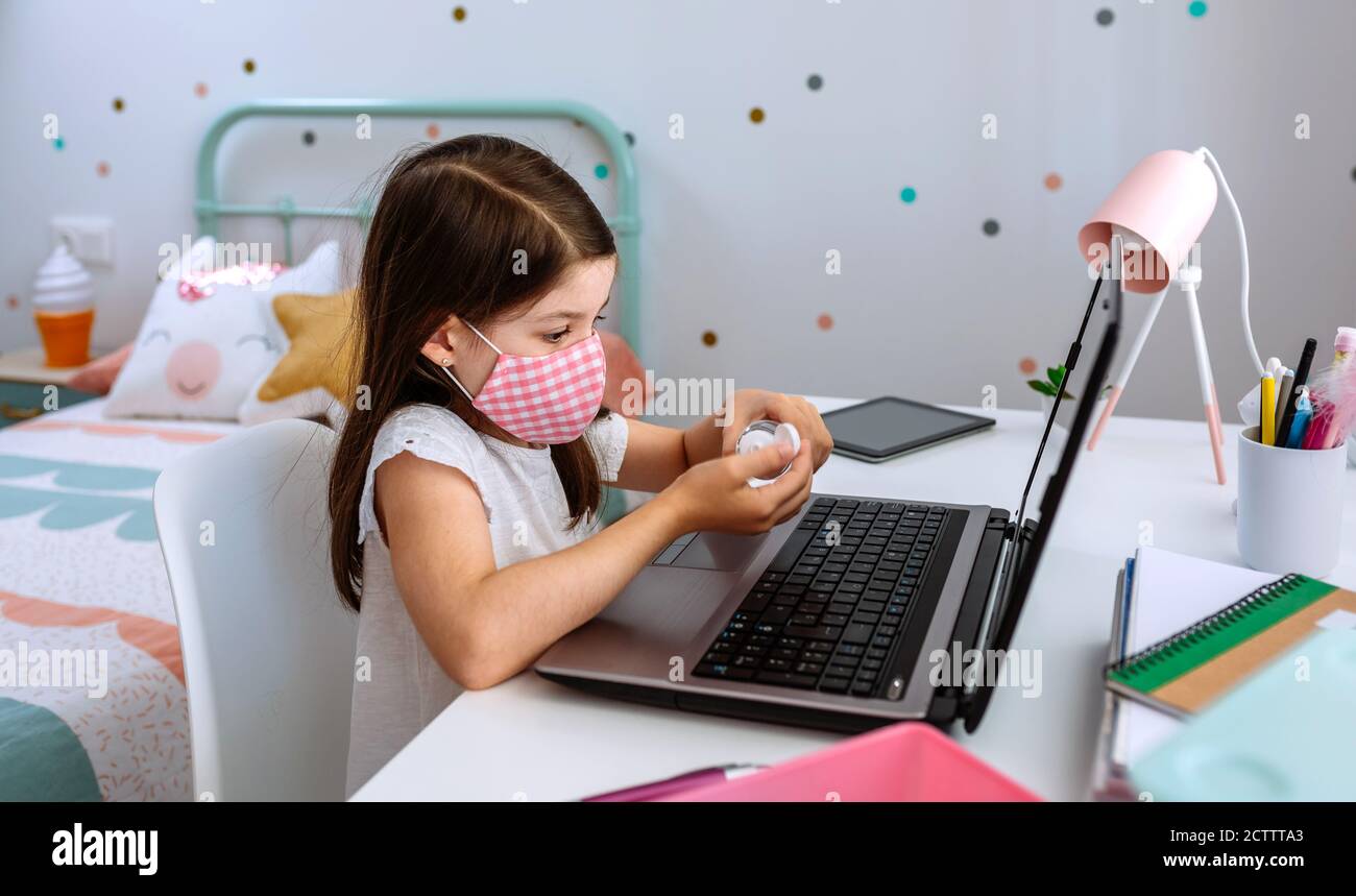 Mädchen Anwendung Hand Desinfektionsmittel während des Studiums mit Laptop Stockfoto