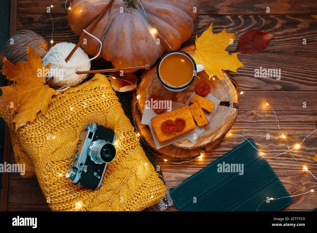 Konzept von Thanksgiving, Halloween oder Weihnachten. Kakao, frisch gebackener Kuchen, getrocknete Aprikosen, auf einem Holztablett. Orange Strickpullover, Vintage-Kamera, großer Kürbis, Tablette und herbstgelbe Blätter. Stockfoto