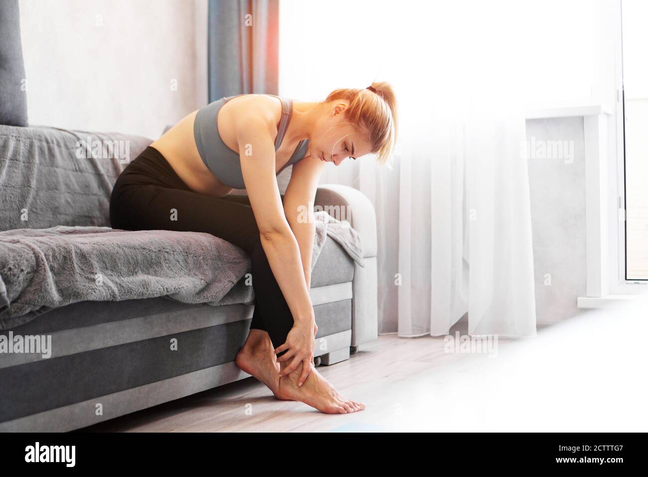 Frau sitzt auf dem Sofa hält ihre Fußverletzung, Gefühl Schmerzen. Gesundheitsfürsorge und medizinisches Konzept. Stockfoto