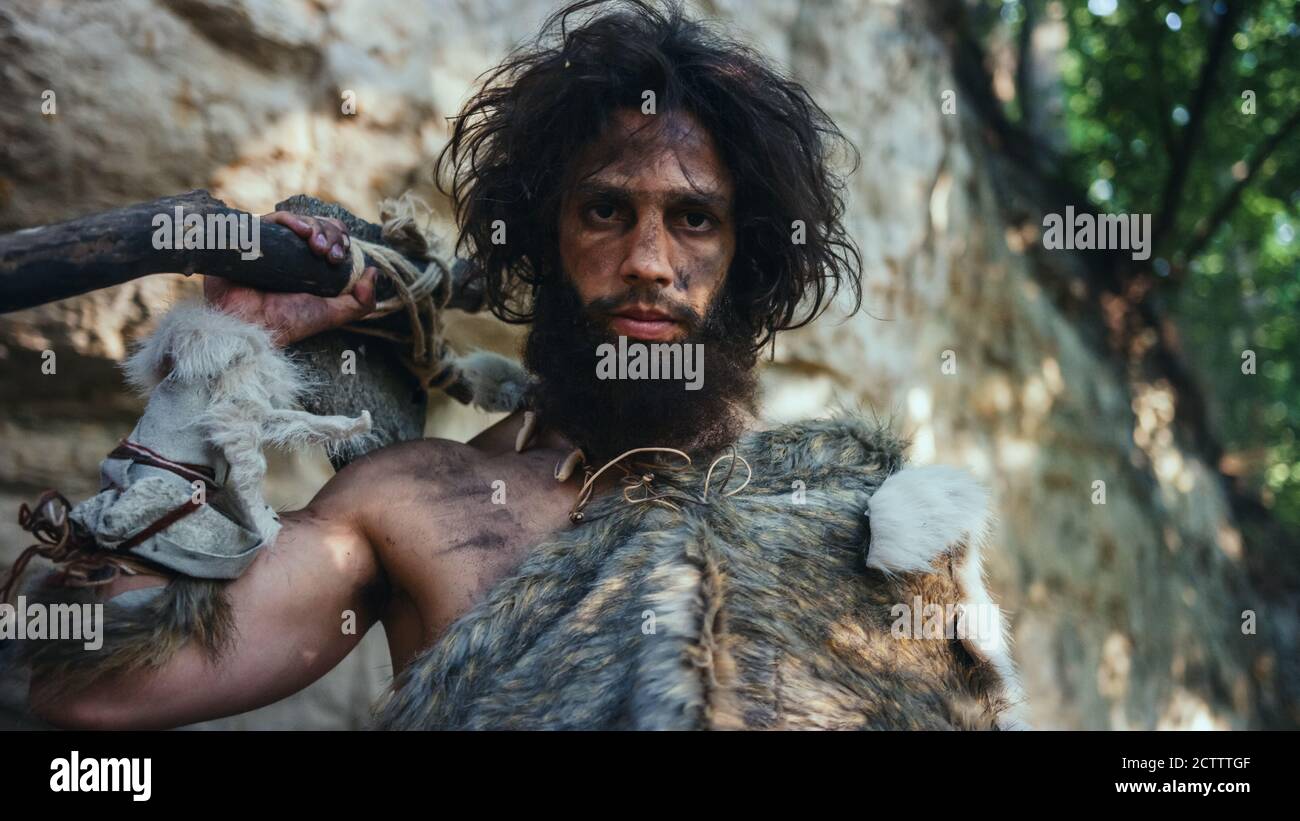 Portrait des uralten Höhlenmenschen mit Tierhaut Holding Stein getippten Hammer. Prähistorische Neanderthal Hunter posiert mit primitiven Jagd in der Stockfoto