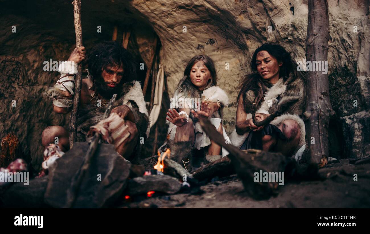 Stamm der prähistorischen PrimitiveJäger und Sammler mit Tierfelle Leben in einer Höhle bei Nacht. Neanderthal oder Homo Sapiens Familie versucht, warm zu werden Stockfoto