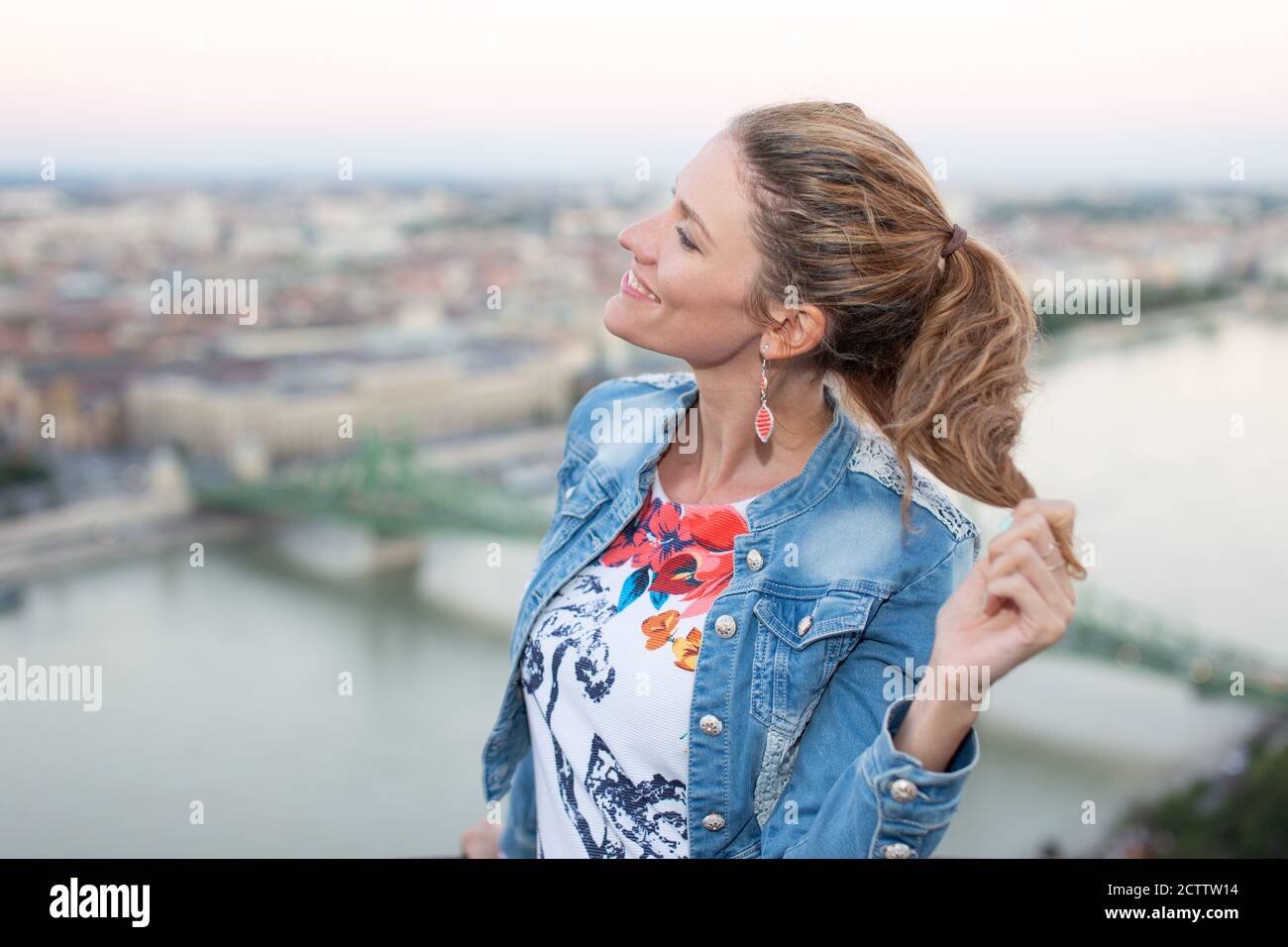 Fröhliche 30s städtische Frau hält Haare in Budapest Panorama, Ungarn Stockfoto