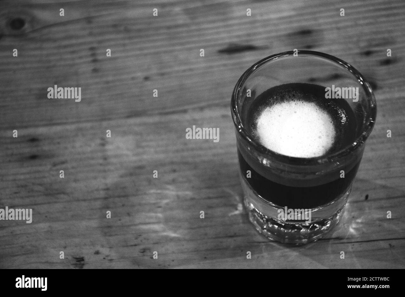 Starker Macchiato-Kaffee in kleinem Glas auf Holztisch. Reflexionen. Bleiben Sie konzentriert Konzept. Schwarzweißfoto Stockfoto