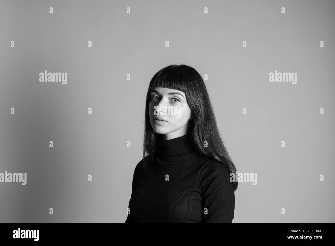 Studio-Porträt einer hübschen Brünette Frau, trägt gefalteten schwarzen Polo-Ausschnitt Pullover, Blick auf die Kamera, vor einem schlichten grauen Hintergrund Stockfoto
