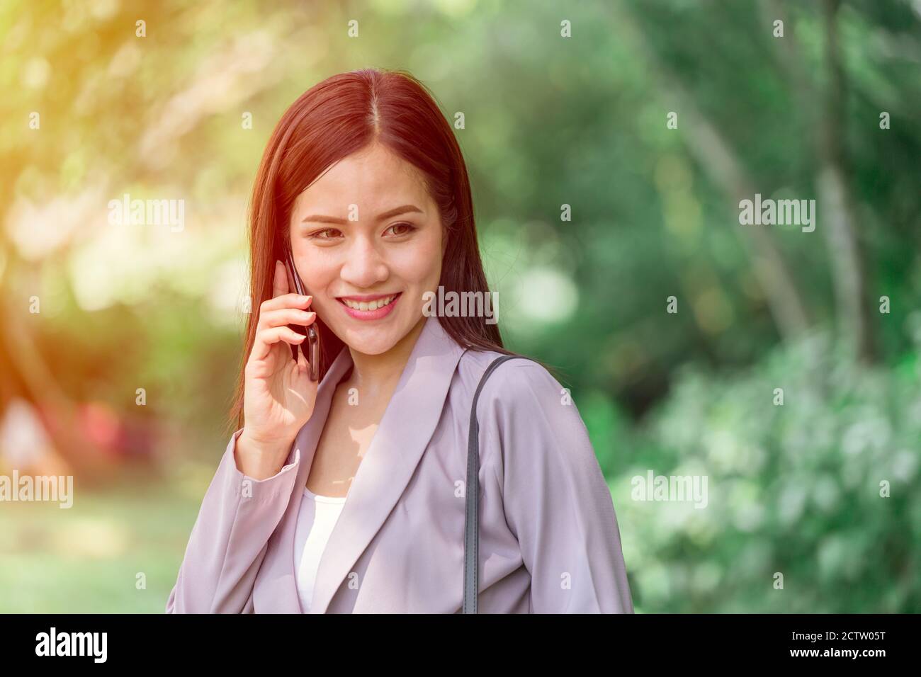 Asiatische Geschäftsfrau mit Telefonieren im Park mit grünen Hintergrund im Freien. Stockfoto