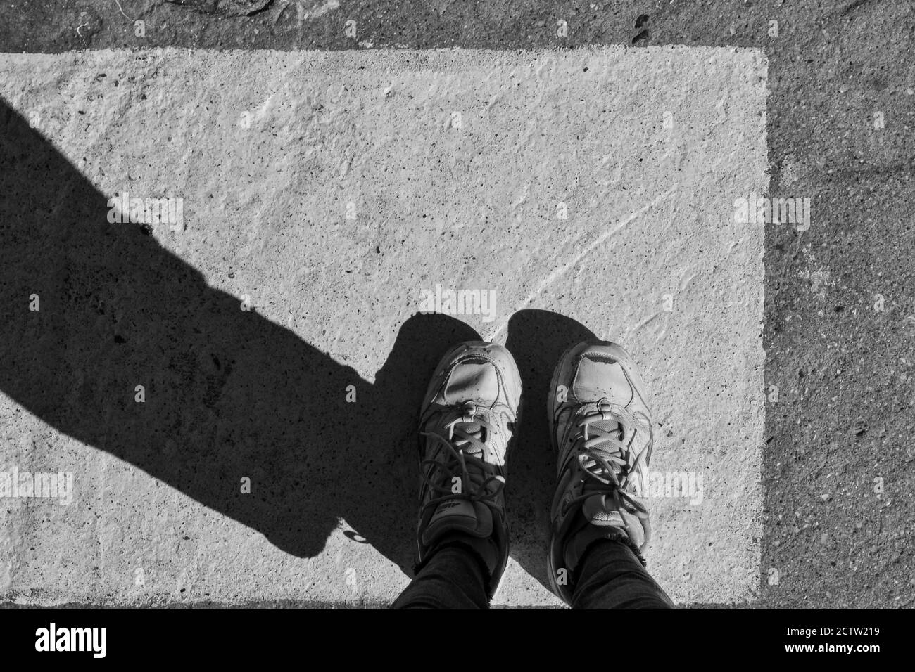 Minimalistische Ästhetik. Schwarz und Weiß. Füße in Schuhen auf einem weißen Quadrat auf dunklem Asphalt. Kreatives Konzept Stockfoto