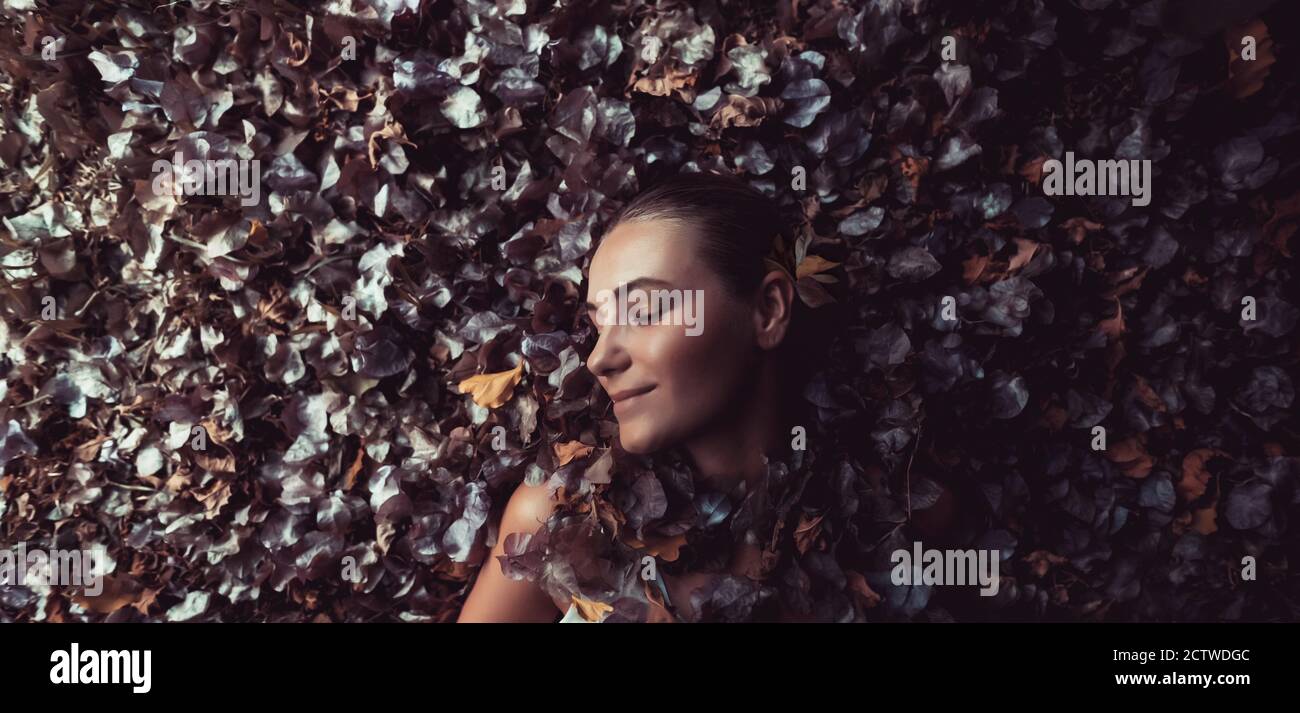 Profil Mode Porträt eines schönen sanften Mädchen liegend im Stapel von trockenen Baumblättern und Blumen. Saisonaler Wechsel. Authentische Schönheit des Herbstes Stockfoto