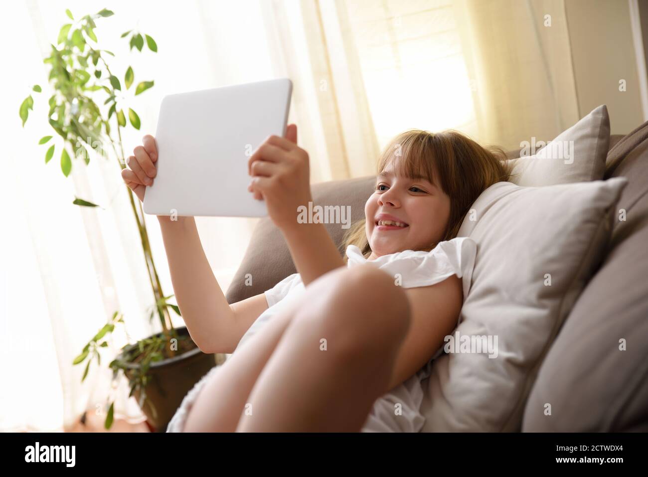 Happy girl gerade Inhalte auf einem Tablet sitzen auf dem Sofa im Wohnzimmer zu Hause Stockfoto