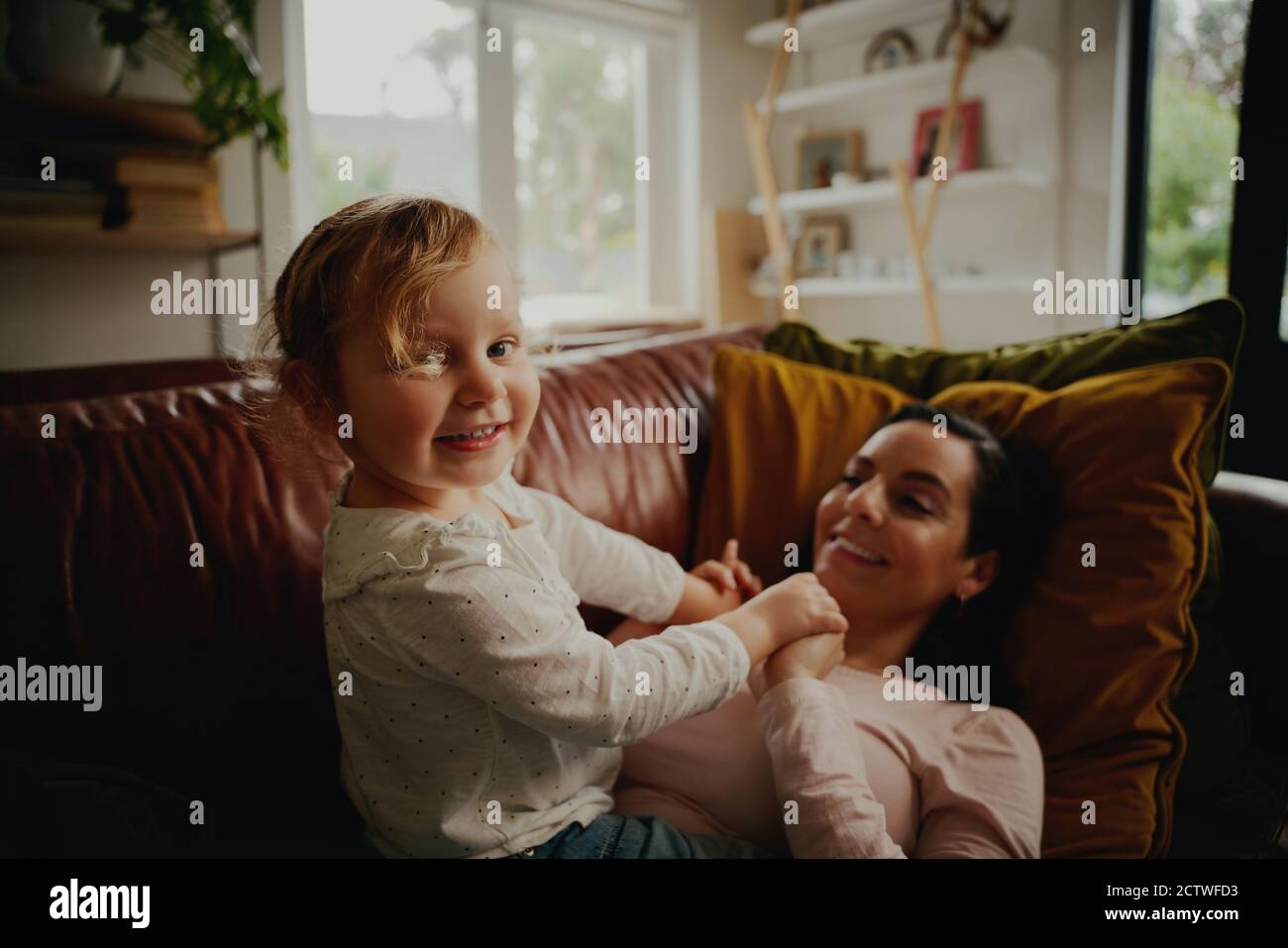 Portrait eines aufgeregten kleinen Kindes, das mit der Mutter spielt, die darauf liegt Couch zu Hause während covid-19 Lockdown Stockfoto