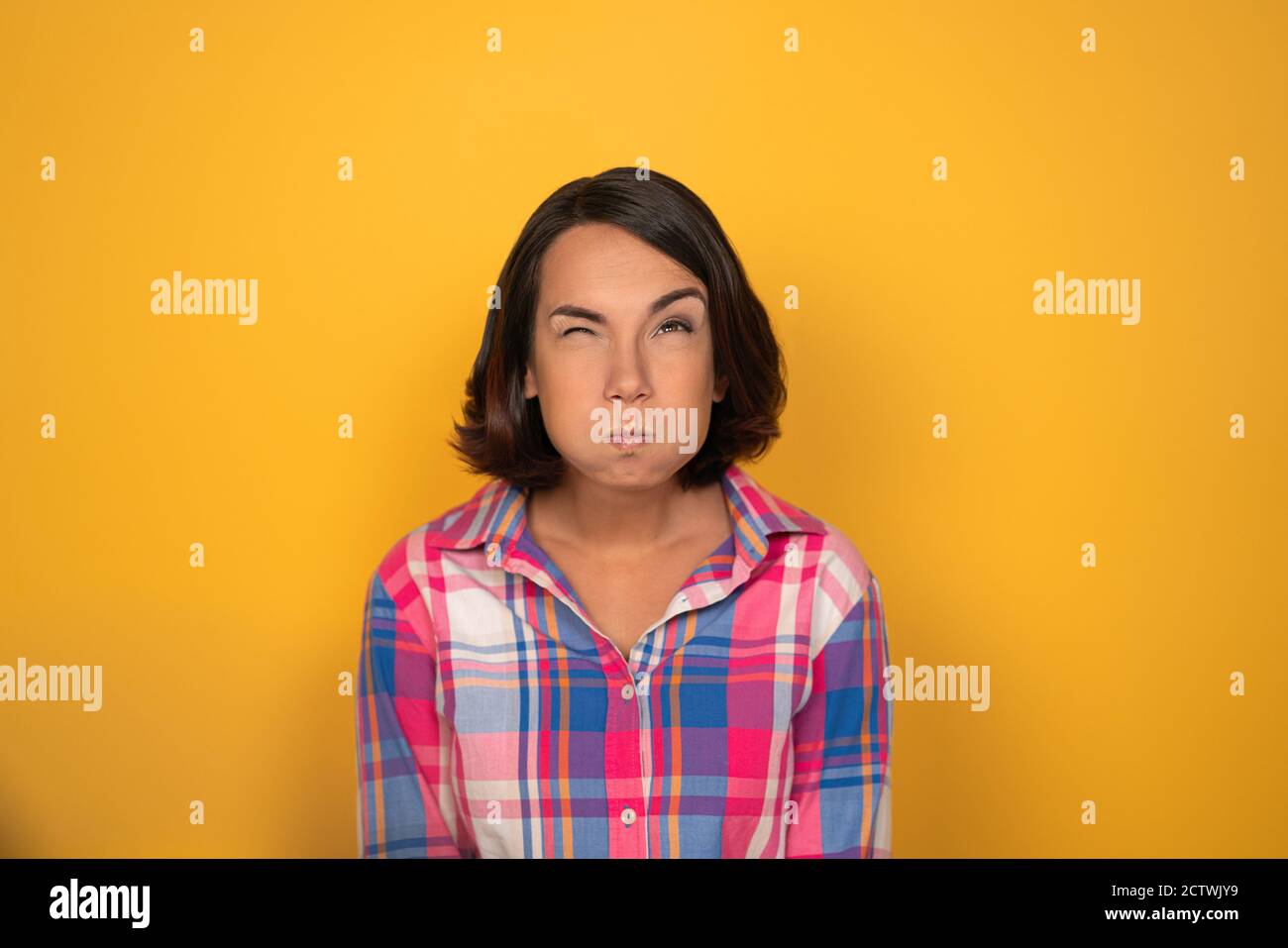 Die junge Frau hatte ihre Wangen auf einem gelben Hintergrund im Studio aufgepumpt. Sie hat ihre Augenbraue gebogen und schaut nach oben. Hochwertige Fotos Stockfoto