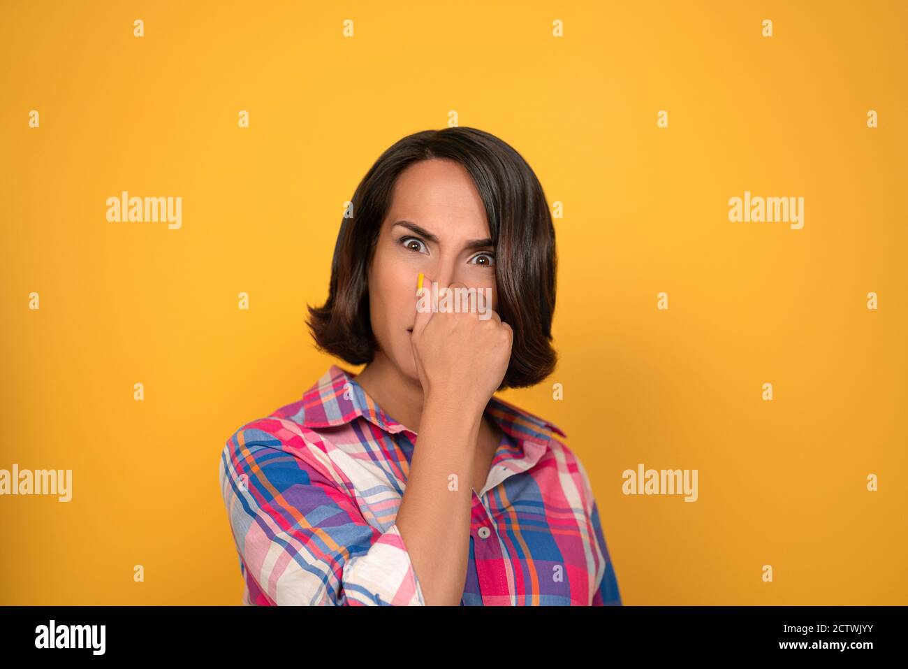Brunette Frau bedeckt ihre Nase mit ihrer Hand. Der unangenehme Geruch des Konzepts. Dreharbeiten im Studio auf gelbem Hintergrund. Hochwertige Fotos Stockfoto