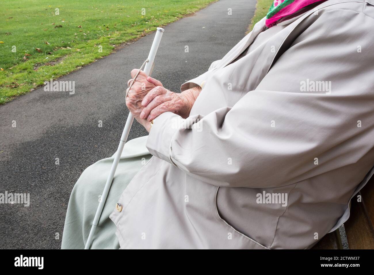 Neunzig Jahre alte Sehbehinderte Dame mit weißen Stock sitzen auf Bank im öffentlichen Park. England, UK Stockfoto