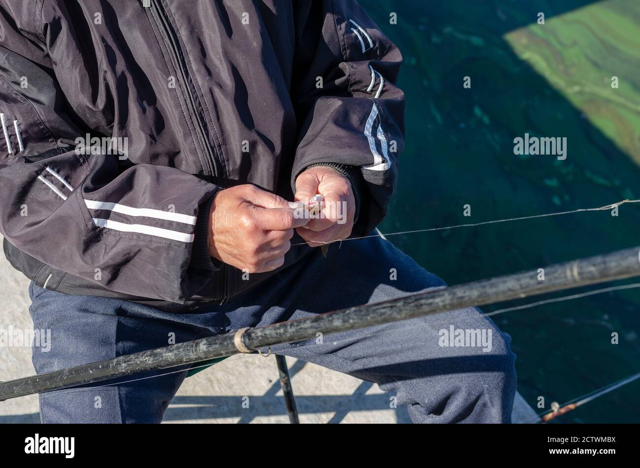 Ein 70-75-jähriger Mann entfernt einen kleinen Fisch aus dem Haken. Nahaufnahme von faltigen Händen mit einem Fang in der Faust. Aktiver Lebensstil älterer Menschen. Selektiv Stockfoto