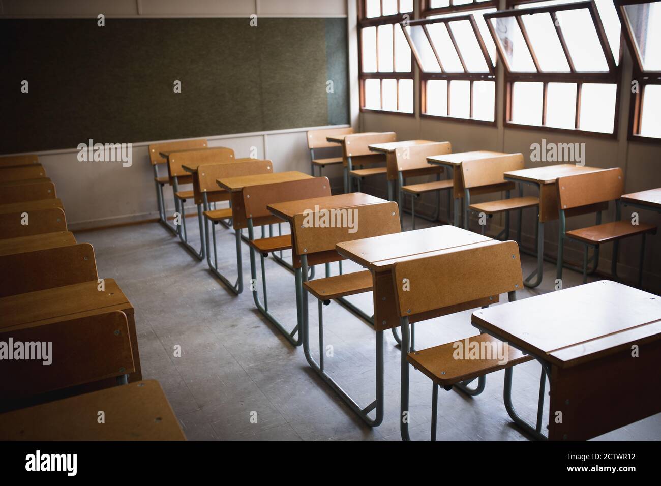 Seitenansicht eines leeren Klassenzimmers, mit Schreibtischen in Formation und Tafel dahinter, mit offenen Fenstern an sonnigen Tagen Stockfoto