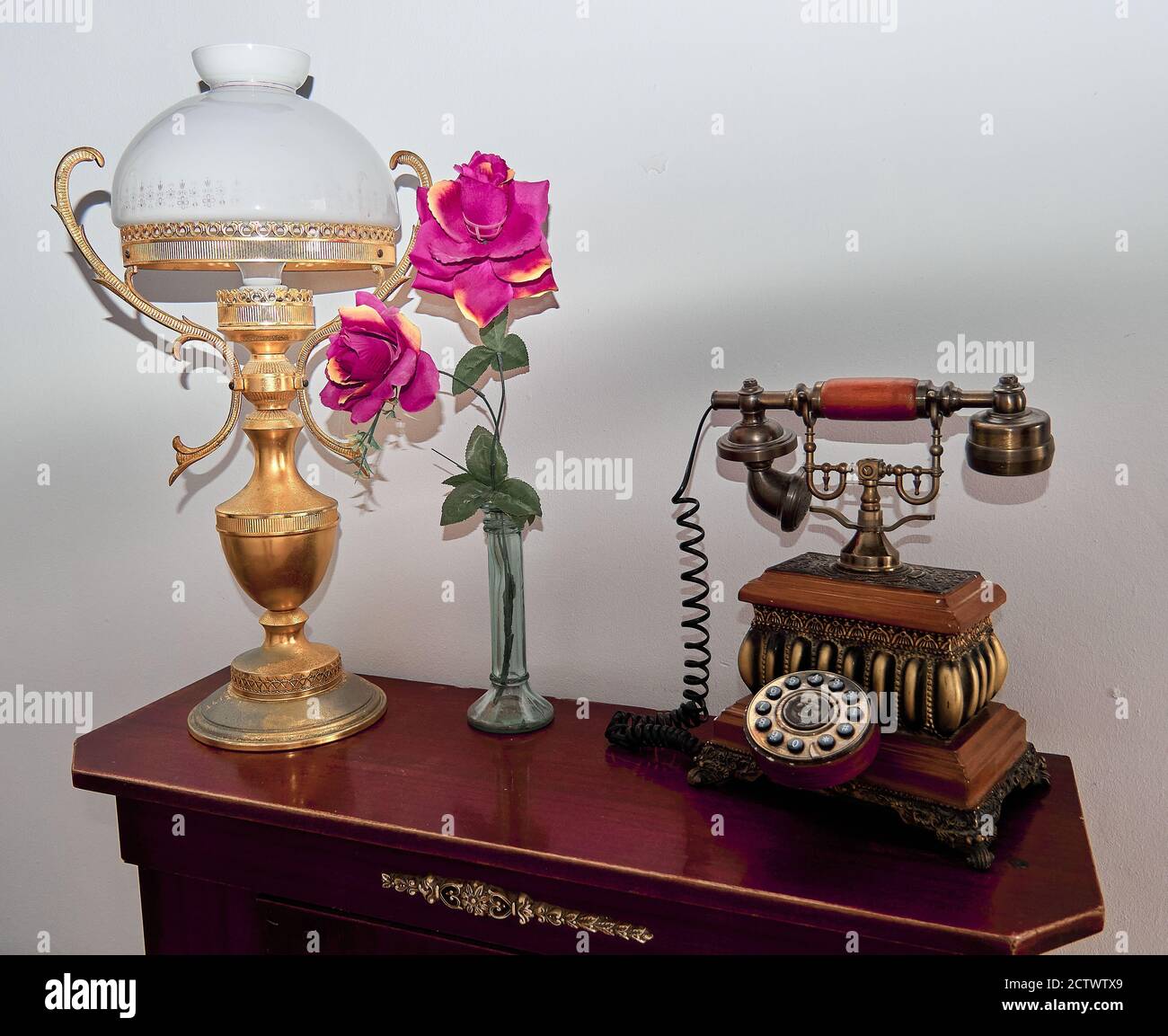 Vintage-Telefon auf dem Flurtisch mit einer Lampe und Rosa Blüten Stockfoto