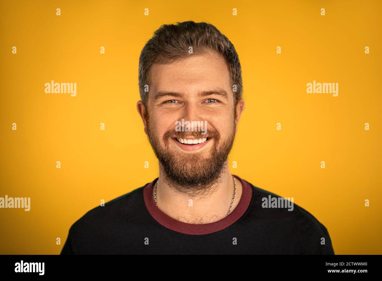 Junger weißer Mann lächelt auf einem gelben Hintergrund im Studio. Mann mit Bart in schwarzer Jacke. Hochwertige Fotos Stockfoto
