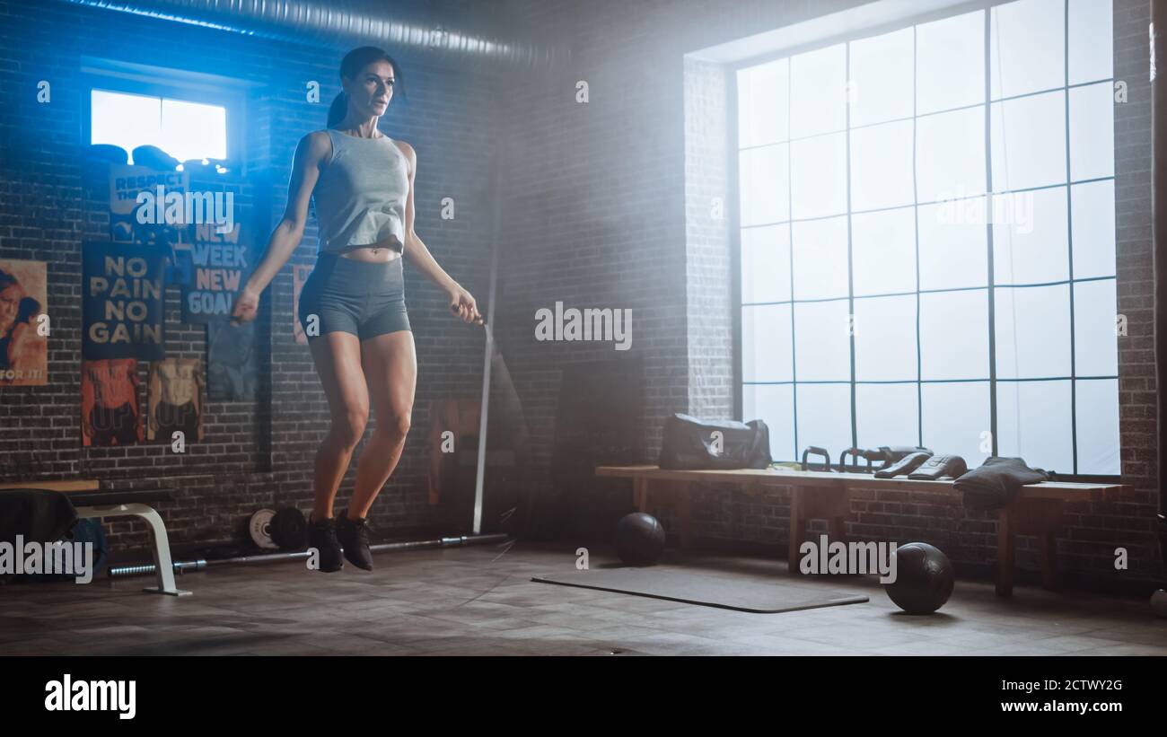 Starke Athletic Frau Übungen mit Springseil in einem Loft-Stil Industrial Gym. Sie konzentriert sich auf ihr intensives Cross Fitness Trainingsprogramm Stockfoto