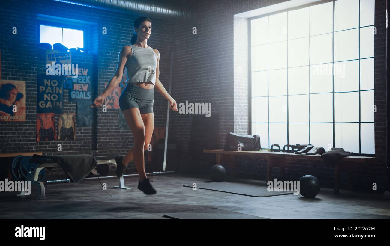 Starke Athletic Frau Übungen mit Springseil in einem Loft-Stil Industrial Gym. Sie konzentriert sich auf ihr intensives Cross Fitness Trainingsprogramm Stockfoto