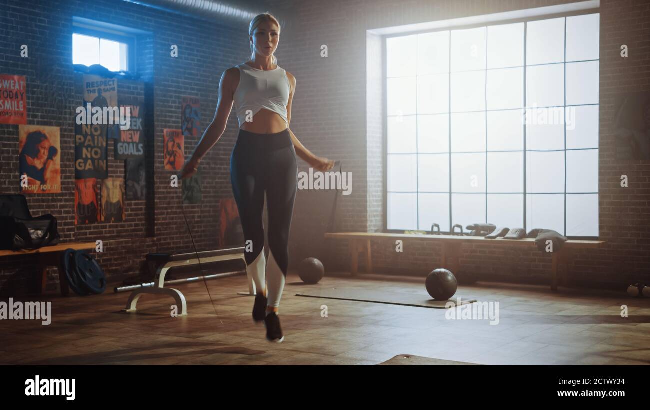 Fit Athletic Blonde Frau Übungen mit Springseil in einem Loft-Stil Industrial Gym. Sie konzentriert sich auf ihr intensives Cross Fitness Trainingsprogramm Stockfoto