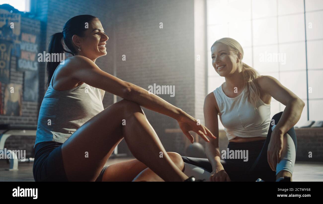 Zwei schöne Fit Athletic Mädchen sitzen auf einem Boden der Industrial Loft Gym. Sie sind mit ihrem Trainingsprogramm zufrieden und sprechen über Sport. Anlage hat Stockfoto