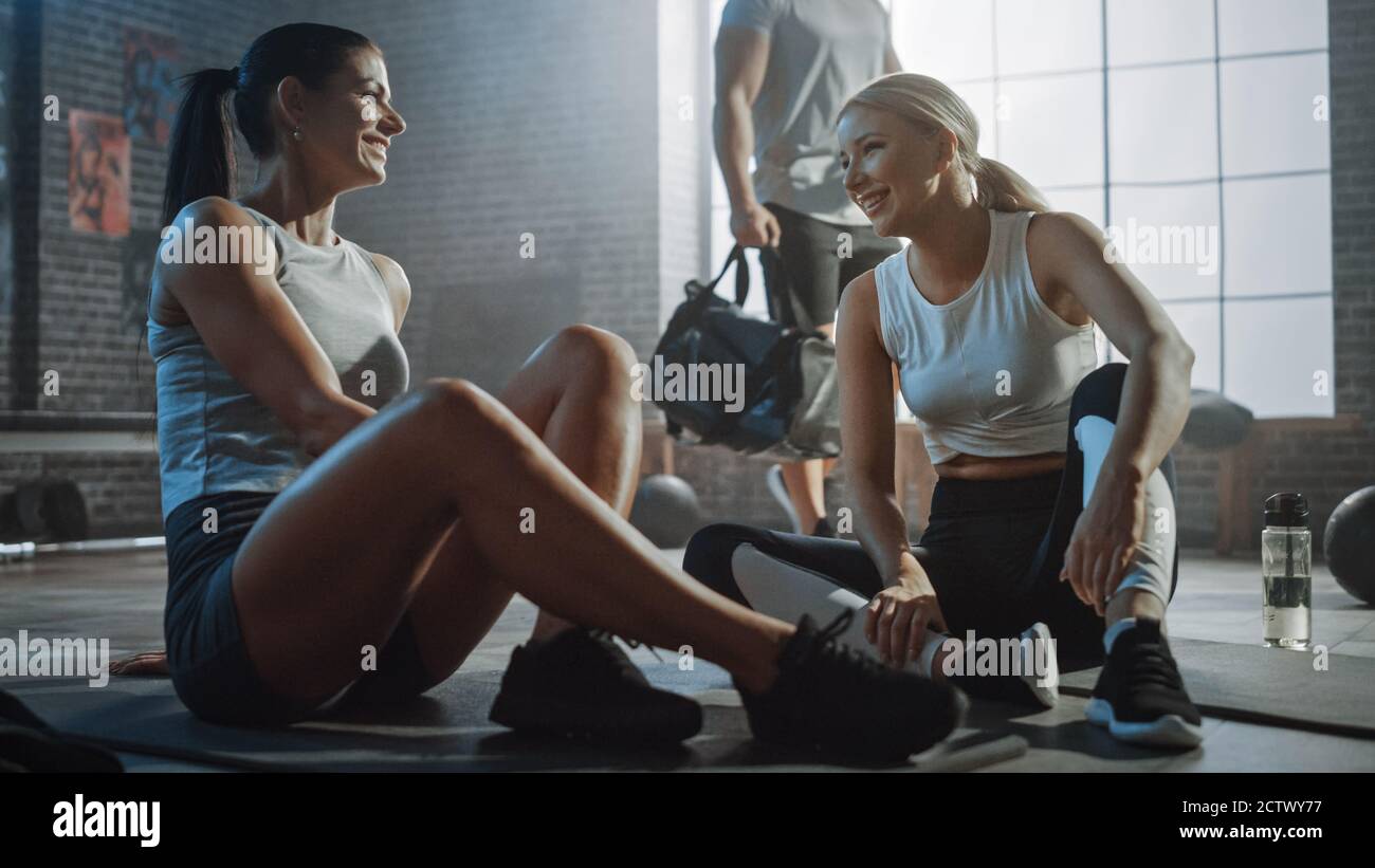 Zwei schöne Fit Athletic Mädchen sitzen auf einem Boden der Industrial Loft Gym. Sie sind mit ihrem Trainingsprogramm zufrieden und geben erfolgreich einen High Five Stockfoto