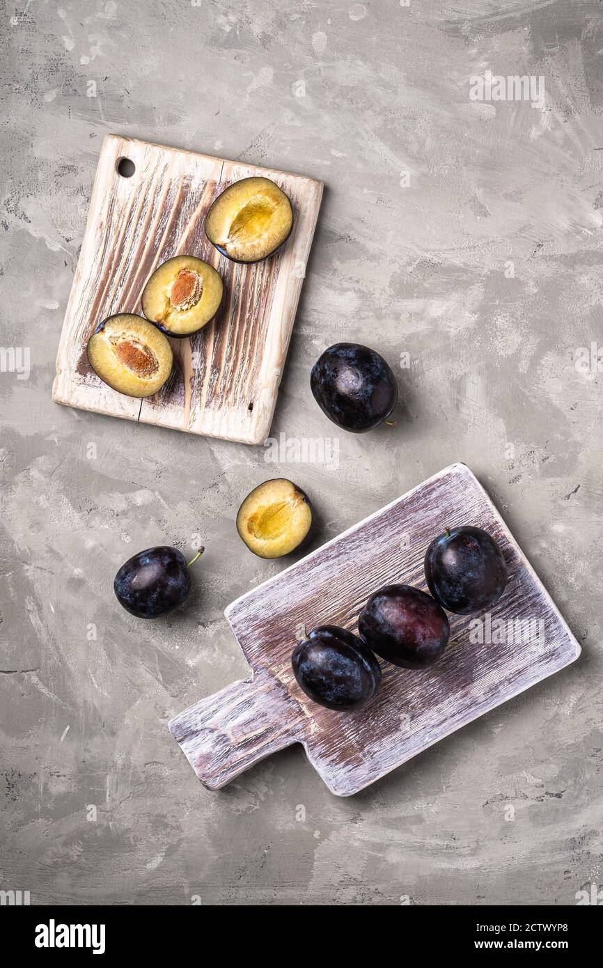 Frische reife Pflaumenfrüchte ganz und in Scheiben geschnitten auf Holzschneidebrettern, Steinbeton Hintergrund, Draufsicht Stockfoto