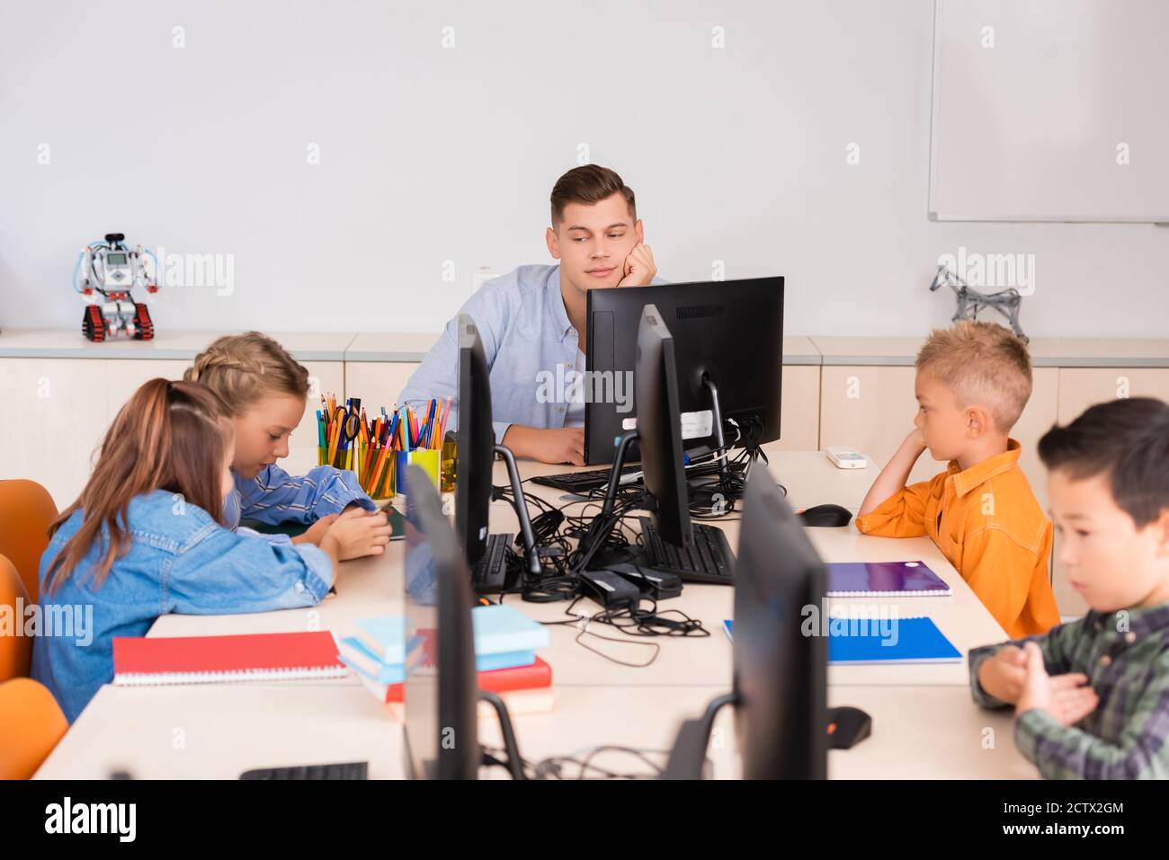 Selektiver Fokus des Lehrers, der multiethnische Schüler in der Nähe von Computern betrachtet In der MINT-Schule Stockfoto