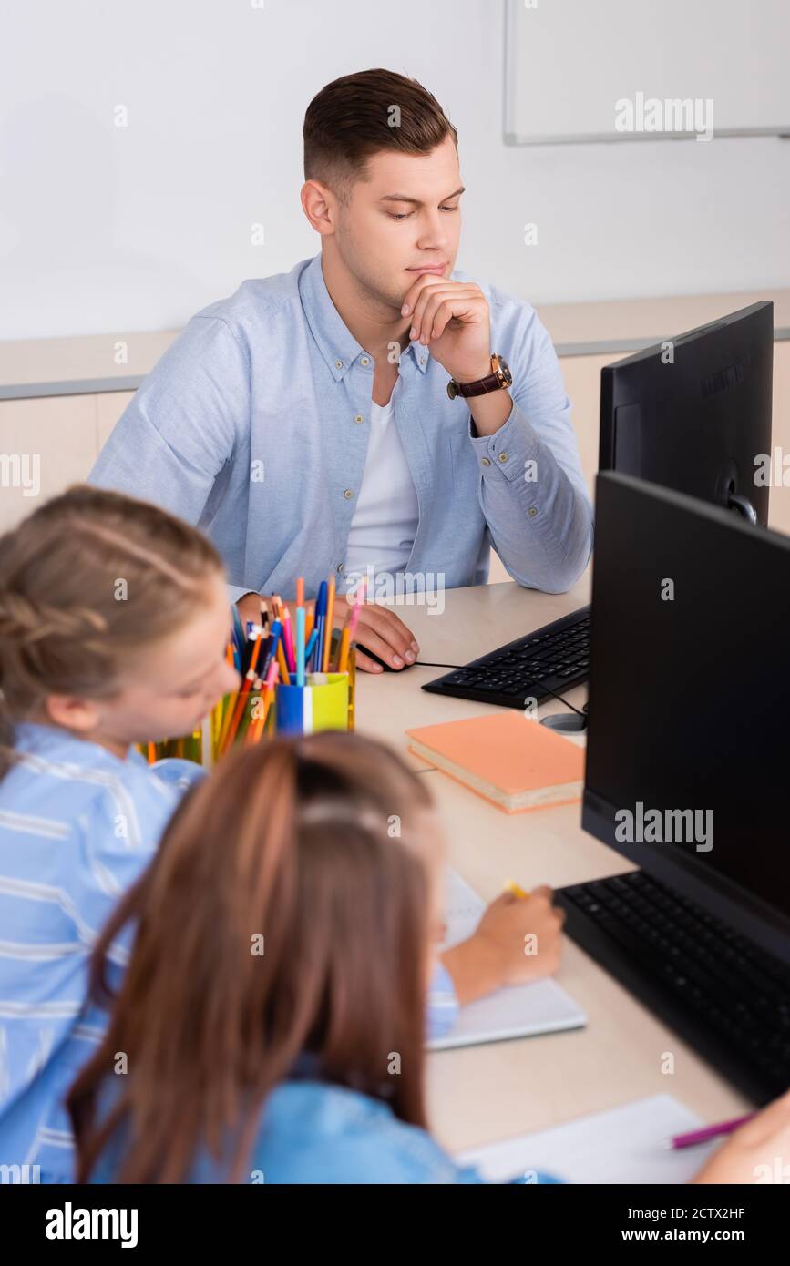 Selektiver Fokus der Lehrer mit Computer in der Nähe von Schülerinnen im Klassenzimmer Stockfoto