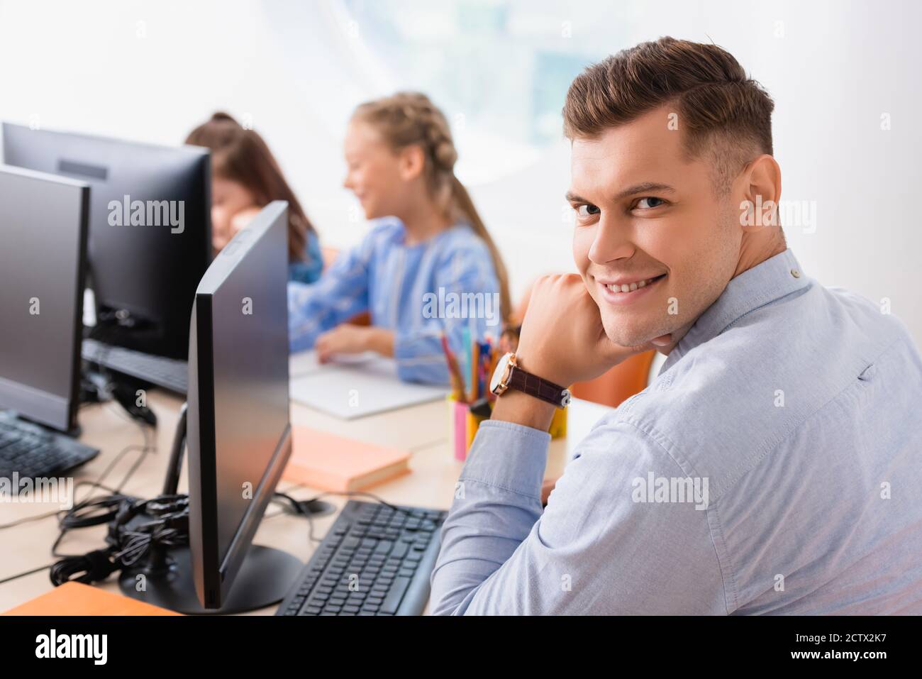 Selektiver Fokus des Lehrers auf Kamera in der Nähe von Computern und Schüler im Klassenzimmer Stockfoto