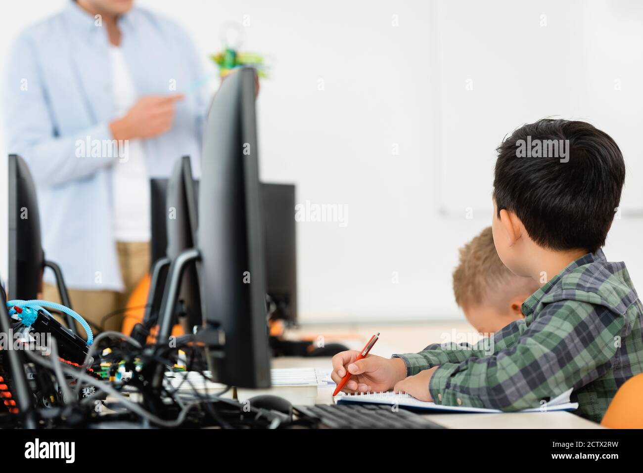 Selektiver Fokus von multiethnischen Schülern, die während des Unterrichts in der Nähe von Computern sitzen Mit Lehrer in der MINT-Schule Stockfoto