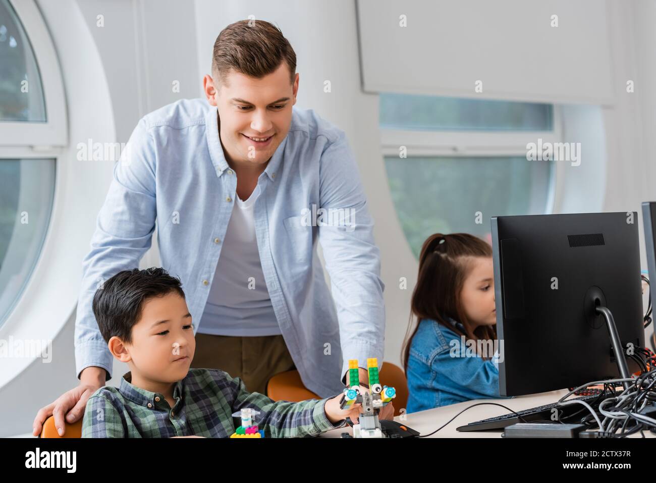 Selektiver Fokus des Lehrers, der in der Nähe des asiatischen Schuljungen steht, der Roboter hält Und Computer im Klassenzimmer Stockfoto