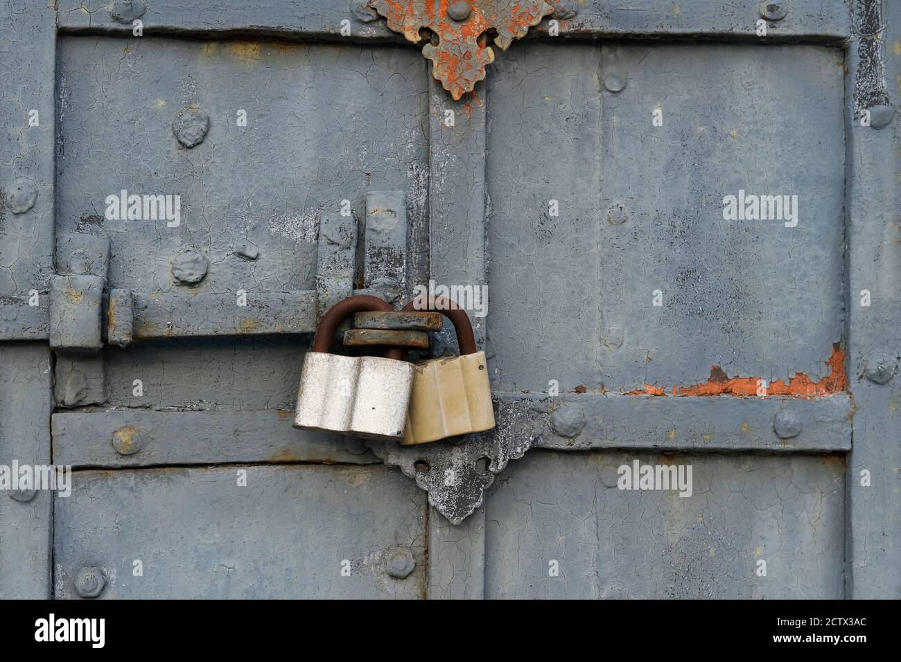 Fragment von alten rissigen Abblätternden und verfallenen Klostertoren mit rostigen geschmiedeten Überzügen und modernen Vorhängeschlössern. Stockfoto
