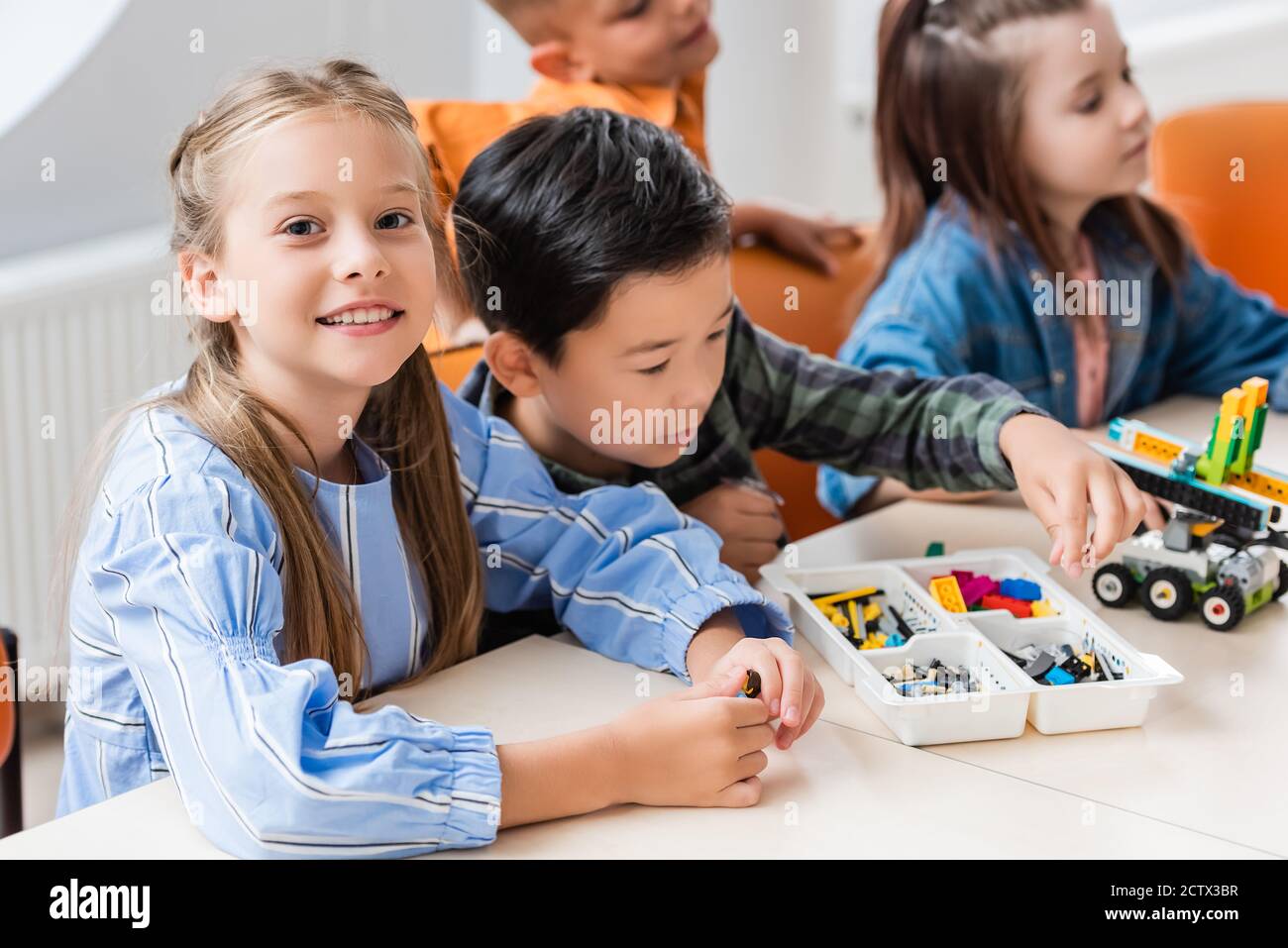Selektiver Fokus von Schulmädchen Blick auf Kamera in der Nähe von multiethnischen Freunden Modellierroboter im Klassenzimmer Stockfoto