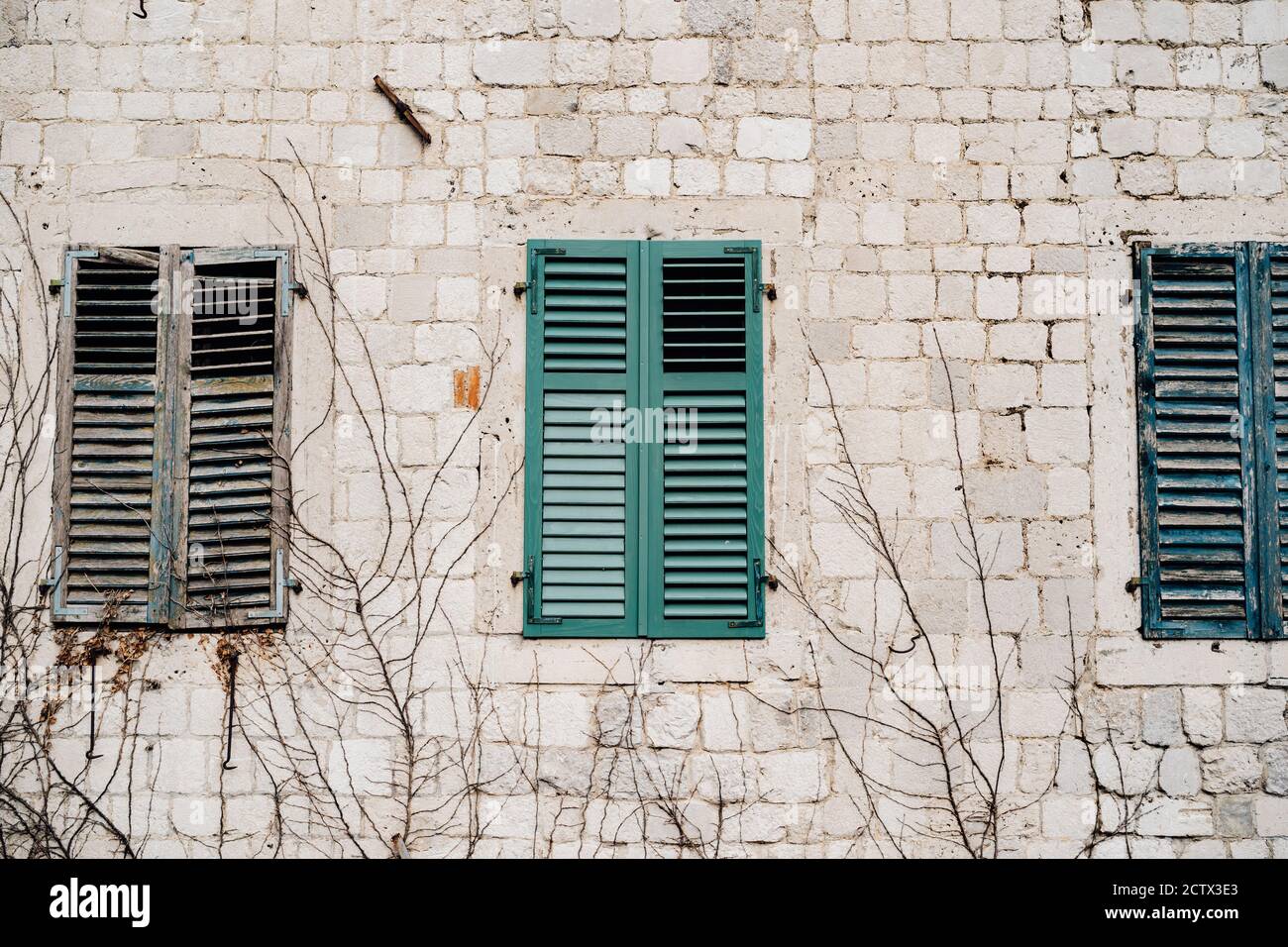 Drei alte Fenster mit geschlossenen grünen Fensterläden an einer Ziegelwand. Stockfoto