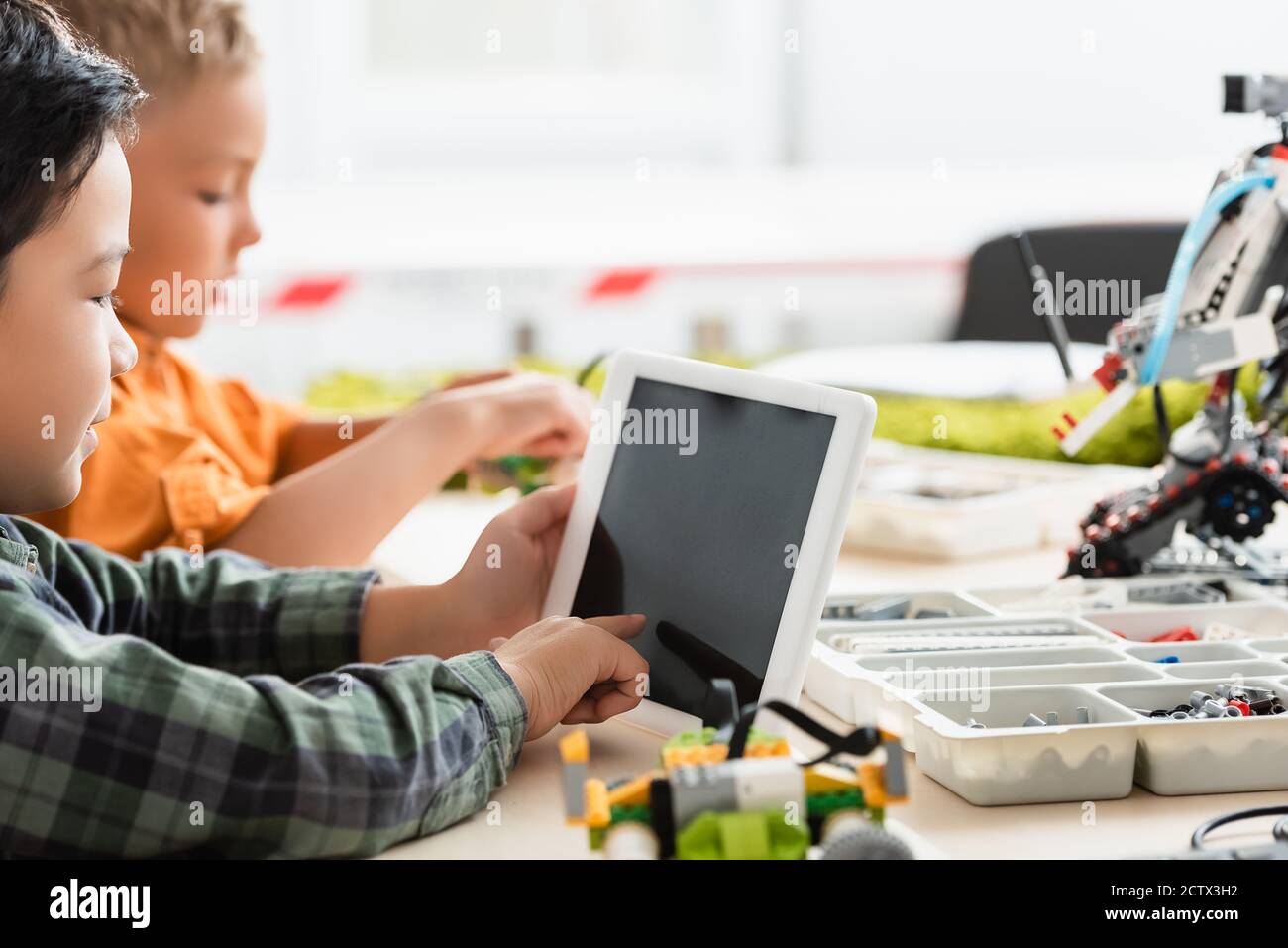 Selektive Fokus der asiatischen Schuljunge mit digitalen Tablet in der Nähe Freund Und Roboter auf dem Tisch in der Schule Stockfoto