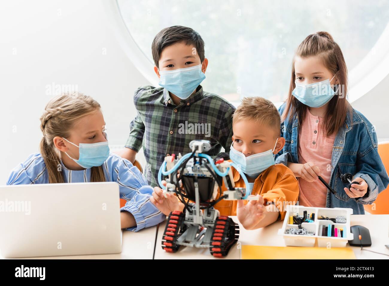 Selektiver Fokus von multiethnischen Klassenkameraden in medizinischen Masken Bau Roboter In der Nähe von Laptops im Klassenzimmer Stockfoto