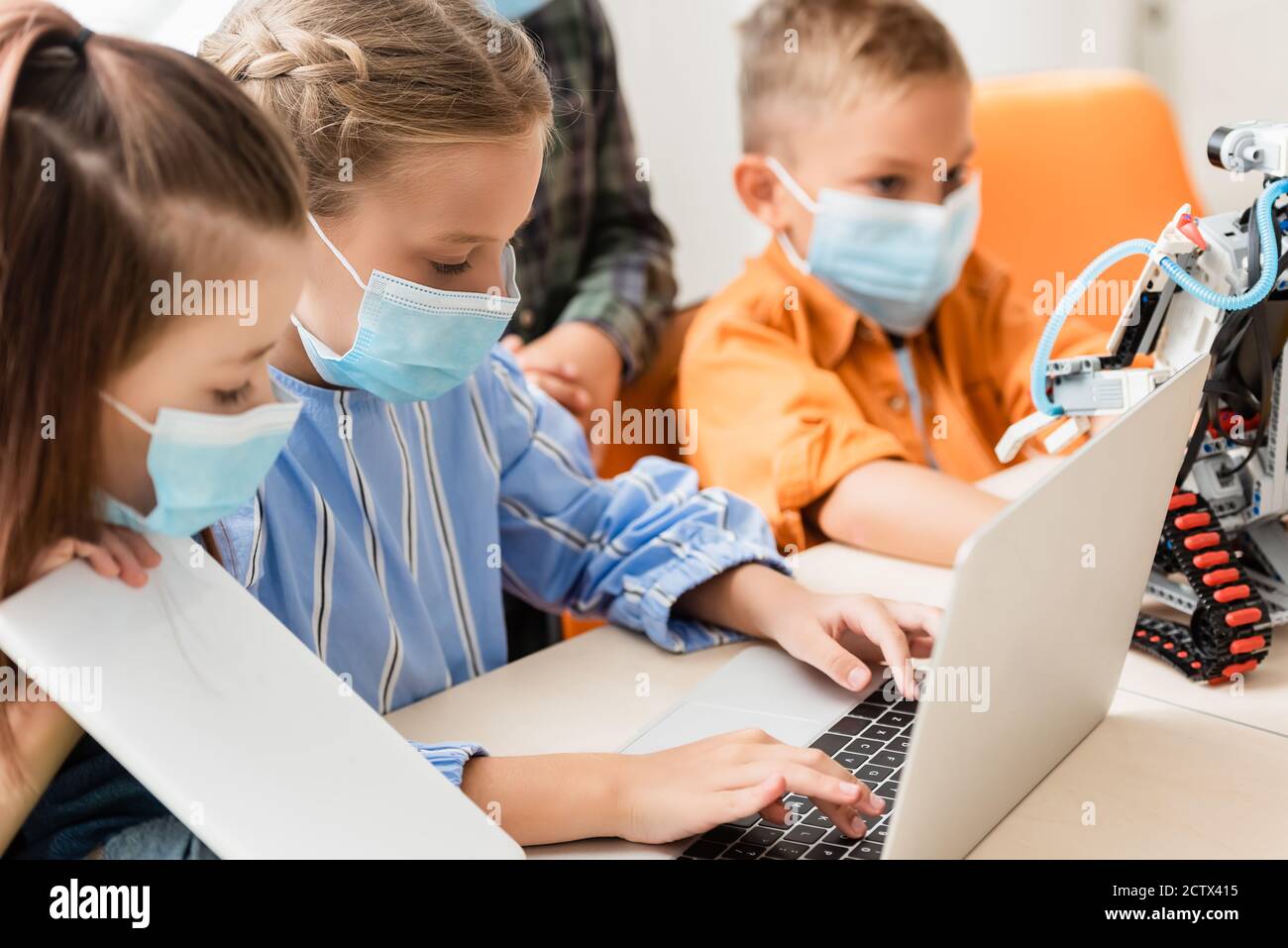 Selektive Fokus von Kindern in medizinischen Masken mit Laptop und Digitales Tablet in der Nähe von Roboter in der Schule Stockfoto