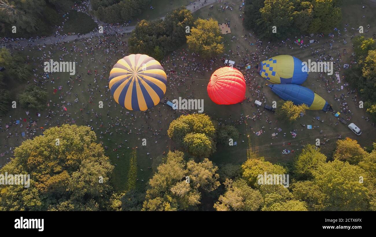 Luftaufnahme von Menschen, die schauen, wie Heißluftballons für einen Sommerabend im Park in der kleinen europäischen Stadt, Kiev Region, Ukraine fliegen vorbereiten Stockfoto